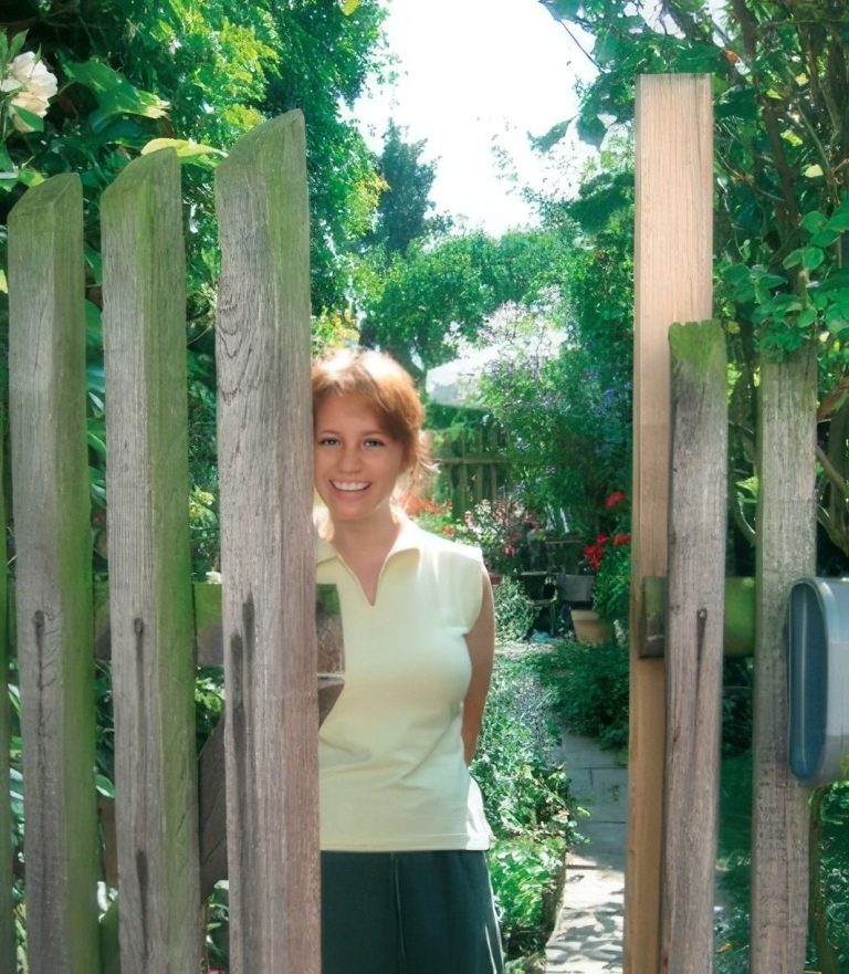 Lächelnde junge Frau öffnet Gartentor